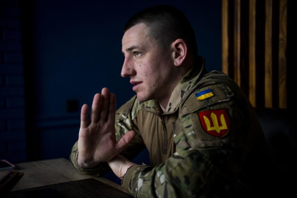 A Ukrainian soldier in uniform raises one hand as he speaks.