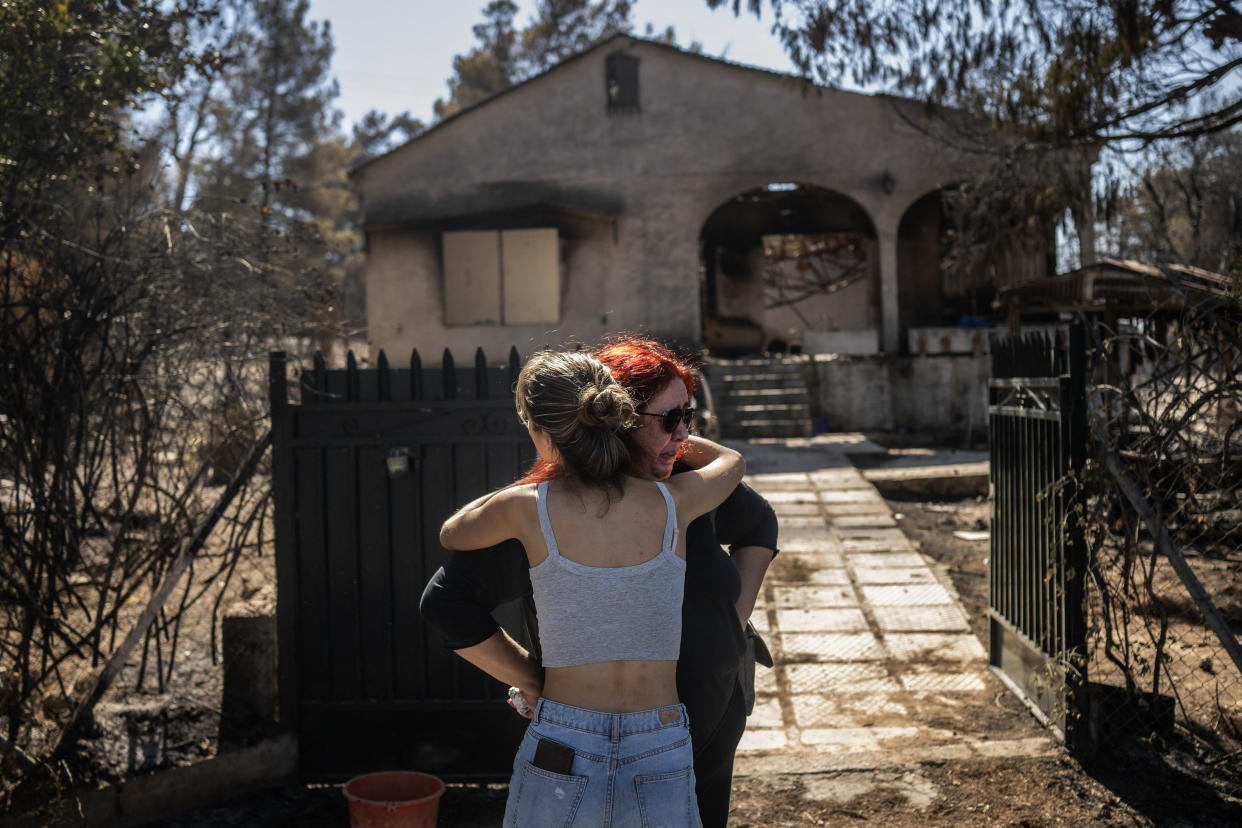 Relatives comfort each other after looking at the damage to their burnt home in a  suburb of Athens on Tuesday. 