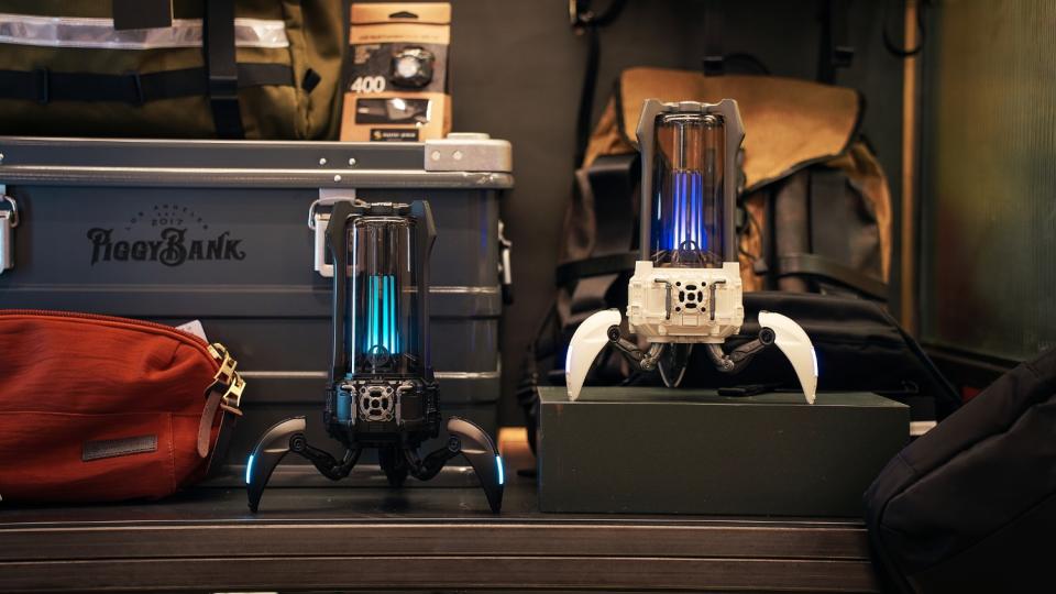 Two Bluetooth speakers that look like bug-like droids from a sci-fi film. They sit on a dark-colored desk with various objects.