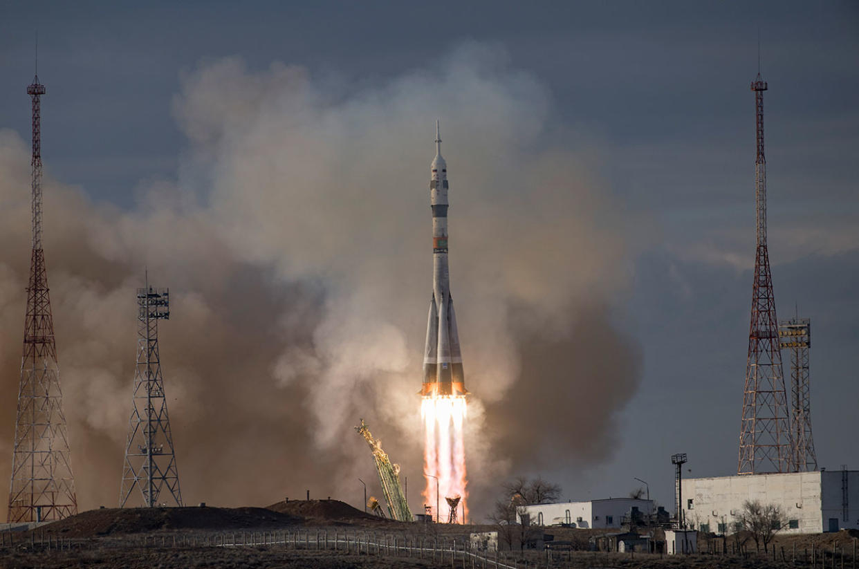  A rocket launches under a cloudy evening sky above a plume of fire of smoke. 