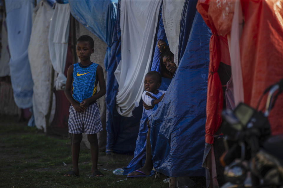 A woman rests with her two children in a makeshift tent at the Devirel camp, six months after a 7.2 magnitude earthquake in Les Cayes, Haiti, Wednesday, Feb. 16, 2022. Thousands of Haitians who lost their homes in the quake remain in camps, living in cramped shelters made of plastic and cloth sheets and corrugated metal. (AP Photo/ Odelyn Joseph)