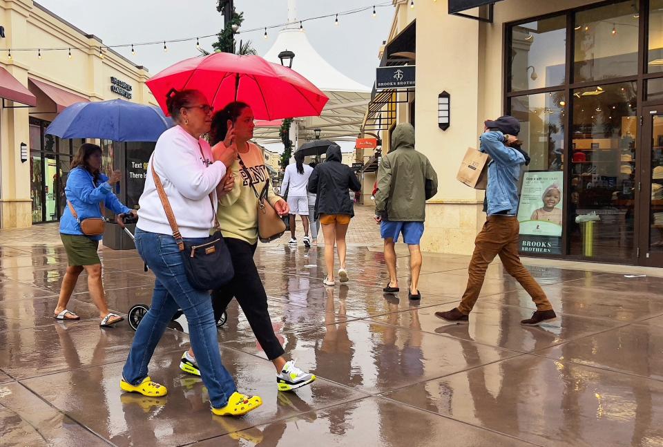 Customers shop in the rain during their visit to the Tanger Outlets in West Palm Beach, Florida on November 20, 2022. 