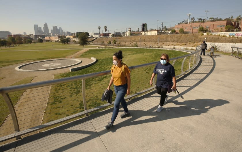 LOS ANGELES, CA - NOVEMBER 19: Jenny Aleman-Zometa, left, Program Director for the Los Angeles River State Park Partners and Xochitl Manzanilla, 78, a nearby resident who serves on a housing and development council walk on the pedestrian bridge overlooking the Los Angeles State Historic Park. A company funded by former Dodgers owner Frank McCourt has proposed a $125 million gondola lift that would fly customers over Los Angeles State Historic Park from Union Station to Dodger Stadium and activists are weighing in. Parents with children and local residents savored the grand opening of the new park in 2017 sandwiched between Chinatown and the L.A. River. Los Angeles State Historic Park, about a 10-minute walk from City Hall, has blossomed into a popular 32-acre urban oasis. Los Angeles State Historic Park on Thursday, Nov. 19, 2020 in Los Angeles, CA. (Al Seib / Los Angeles Times