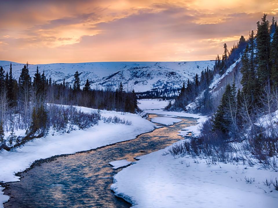 A dramatic sunset illuminates the clear waters of Phelan Creek in early spring in the Alaska Range.