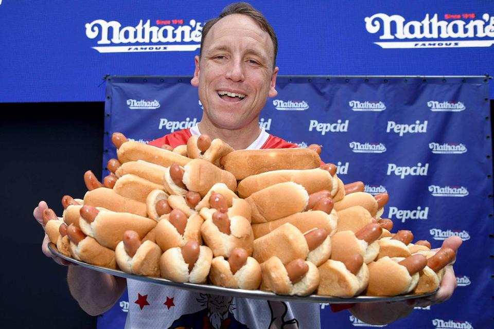 <p>Anthony Behar/Sipa USA</p> Joey Chestnut holding a plate of hot dogs.