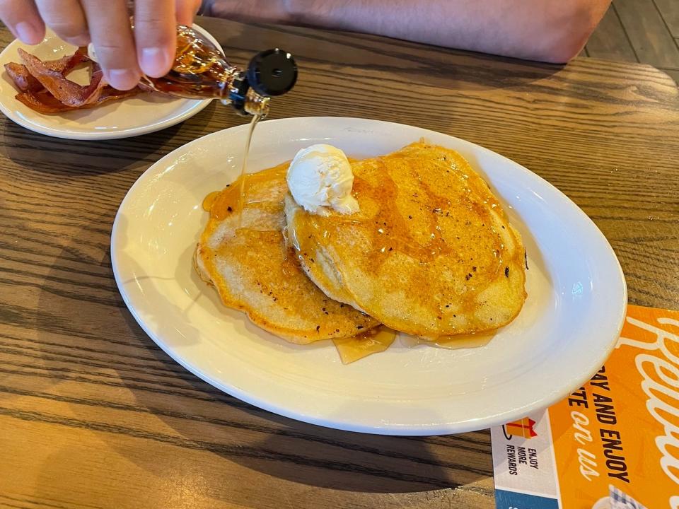 tim pouring syrup over a stack of pancakes from cracker barrel