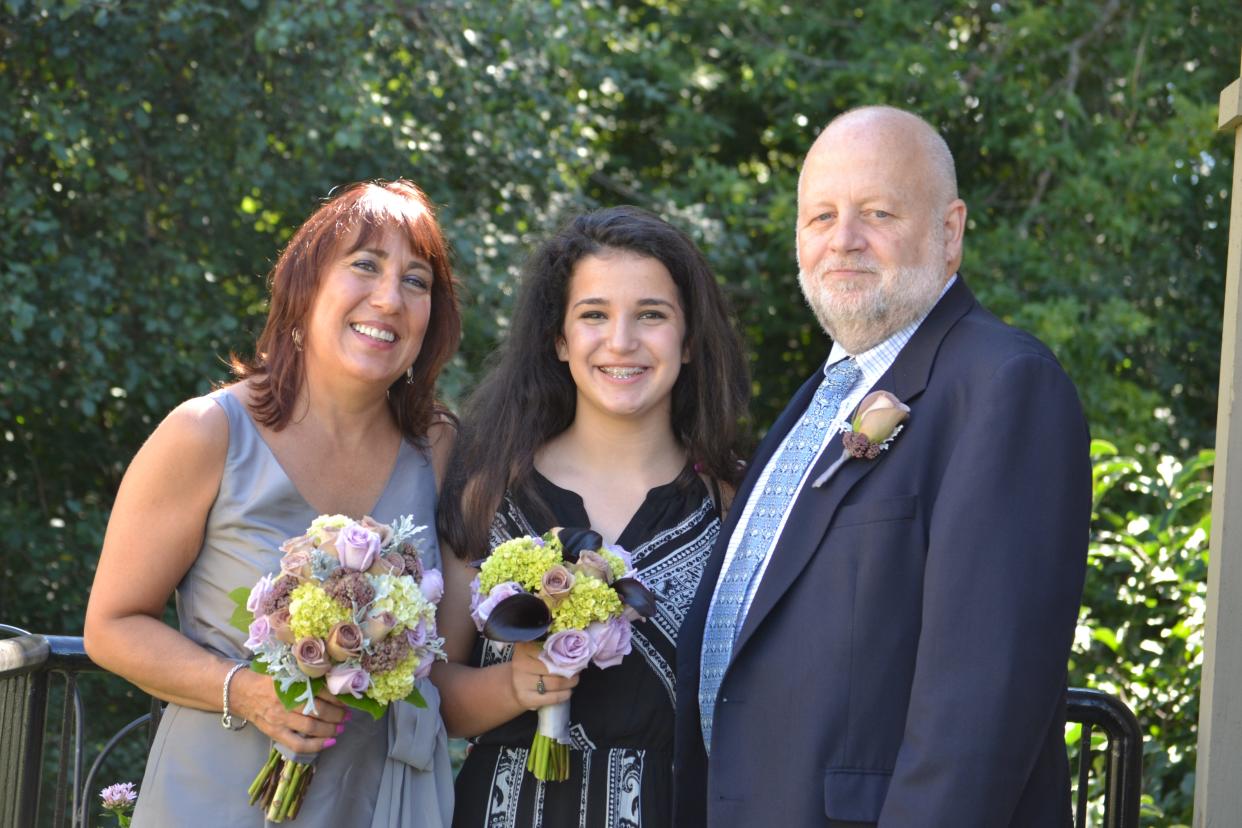 Isabella Ambrosio with her mom and dad. They are dressed up and she and her mom are holding bouquets of flowers.