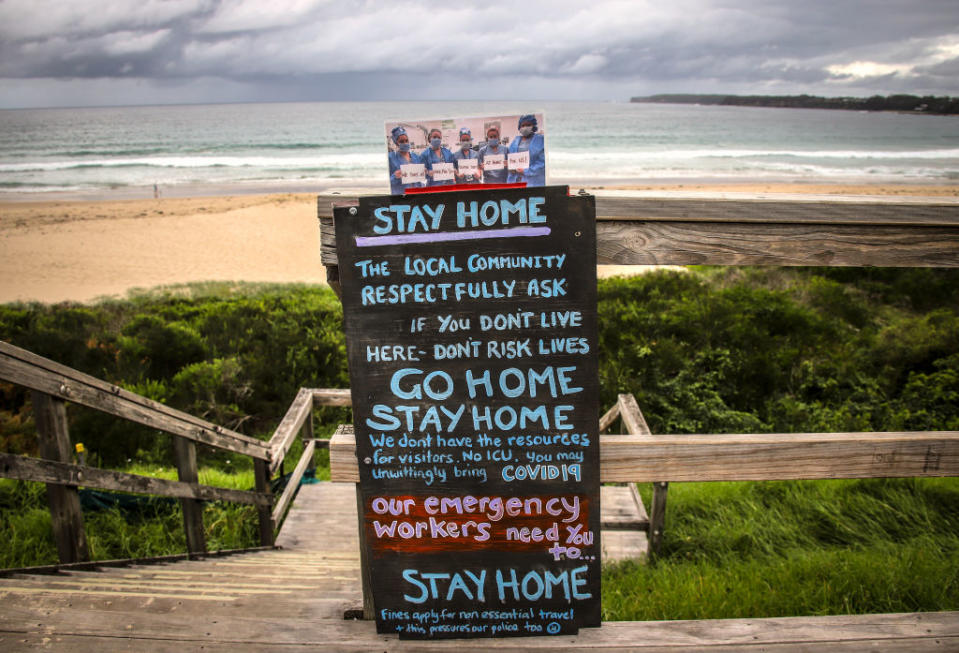 A sign asking people to not travel due to the coronavirus stands at a stairway leading onto Mollymook Beach. Source: Getty