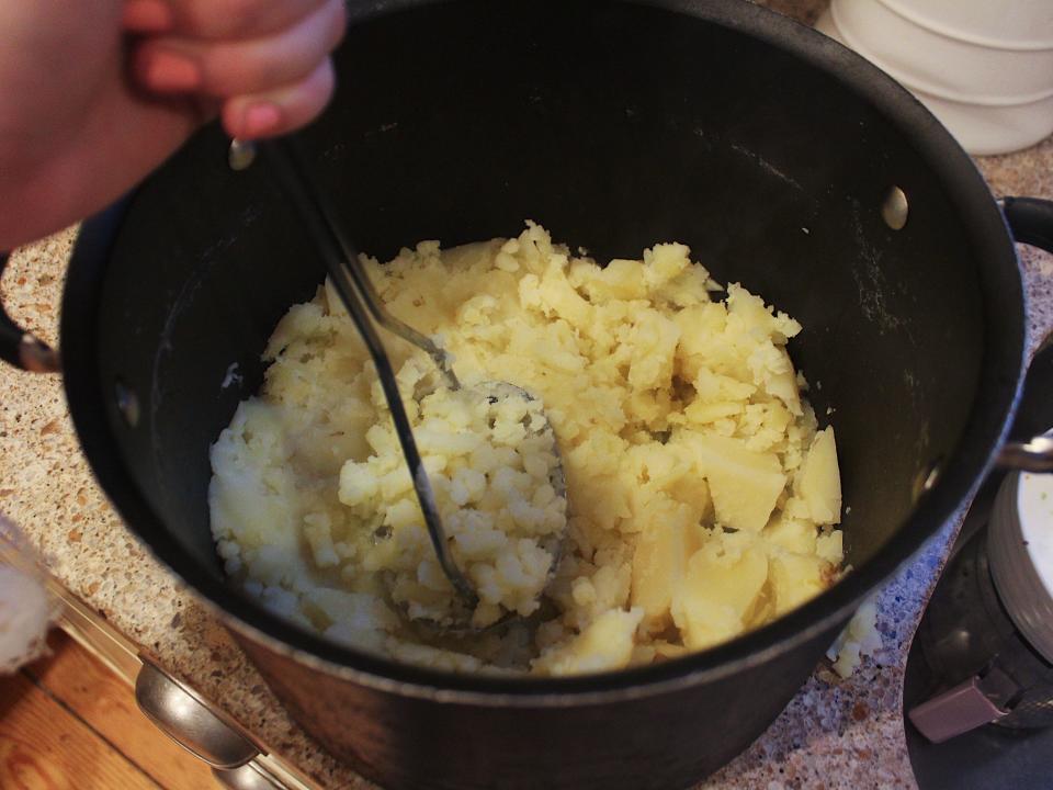 hand mashing potatoes in a black pot