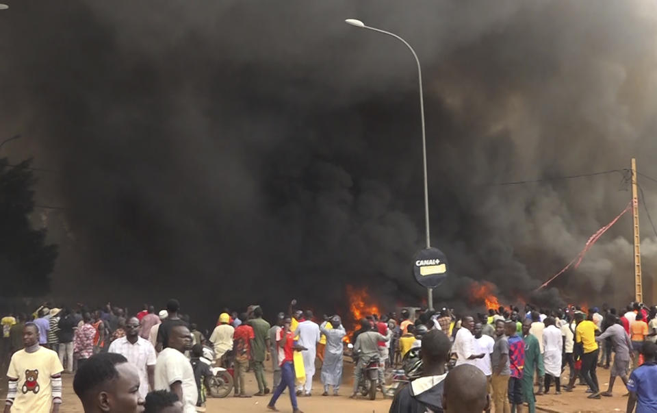 With the headquarters of the ruling party burning in the back, supporters of mutinous soldiers demonstrate in Niamey, Niger, Thursday, July 27 2023. Governing bodies in Africa condemned what they characterized as a coup attempt Wednesday against Niger's President Mohamed Bazoum, after members of the presidential guard declared they had seized power in a coup over the West African country's deteriorating security situation. (AP Photo/Fatahoulaye Hassane Midou)