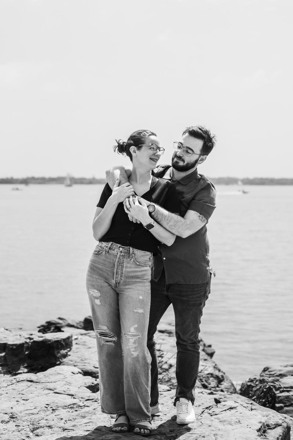 A couple embraces in front of a body of water.