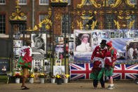 People pose in the Welsh flag as they stand in front of portraits and messages of remembrance for Princess Diana displayed on the gates of Kensington Palace, in London, Wednesday, Aug. 31, 2022. Wednesday marks the 25th anniversary of Princess Diana's death in a Paris car crash. (AP Photo/Alastair Grant)