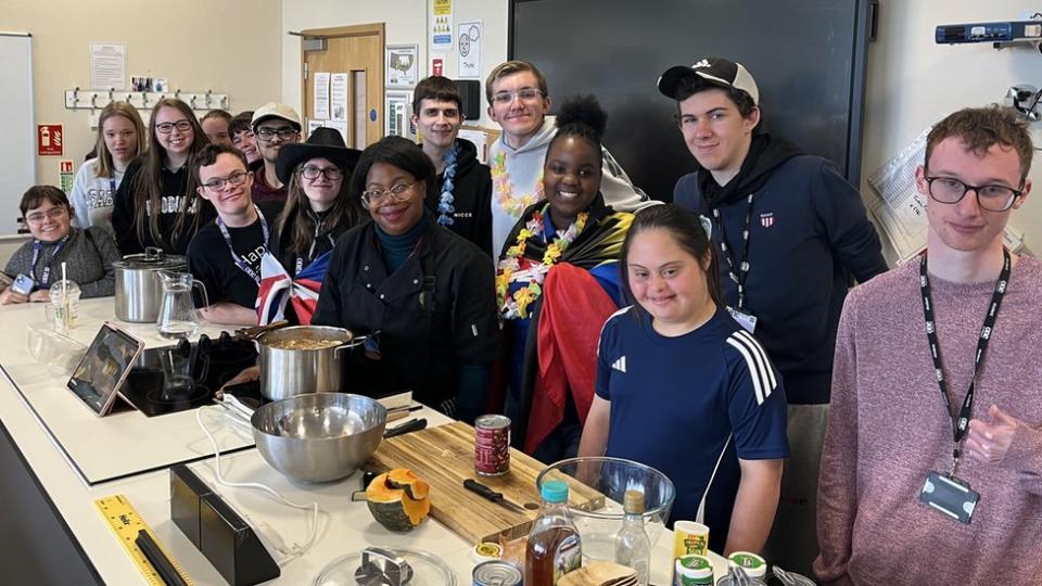 Students stand alongside a chef by a cooking counter top