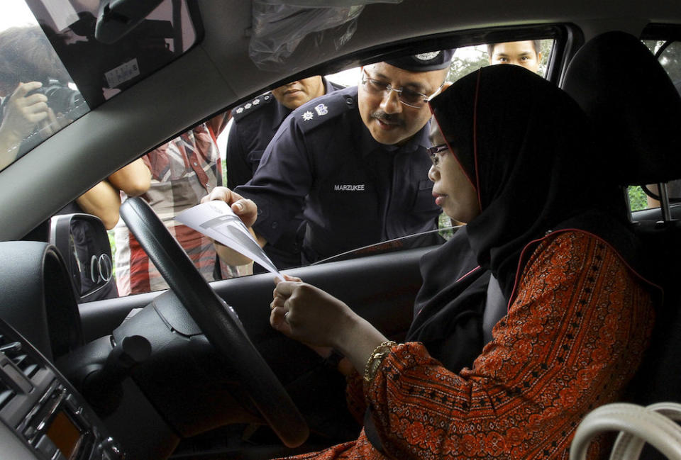 A policeman hands a poster to a motorist bearing a portrait of the missing 15-year-old Franco-Irish girl Nora Anne Quoirin during a search and rescue operation in Seremban August 9, 2019. — Bernama pic