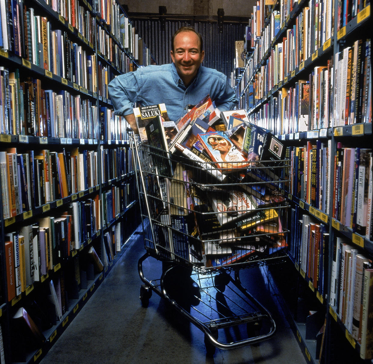 Retrato del empresario estadounidense y CEO de Amazon.com Jeff Bezos posa en un pasillo de estanterías con un carrito de compras lleno de libros y discos compactos, Seattle, Washington, septiembre de 1998. (Foto de Rex Rystedt / The LIFE Images Collection a través de Getty Images / Getty Imágenes) 