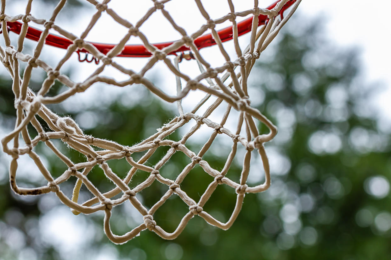 old used basketball hoop with red paint and netting haning in outdoor setting on overcast day