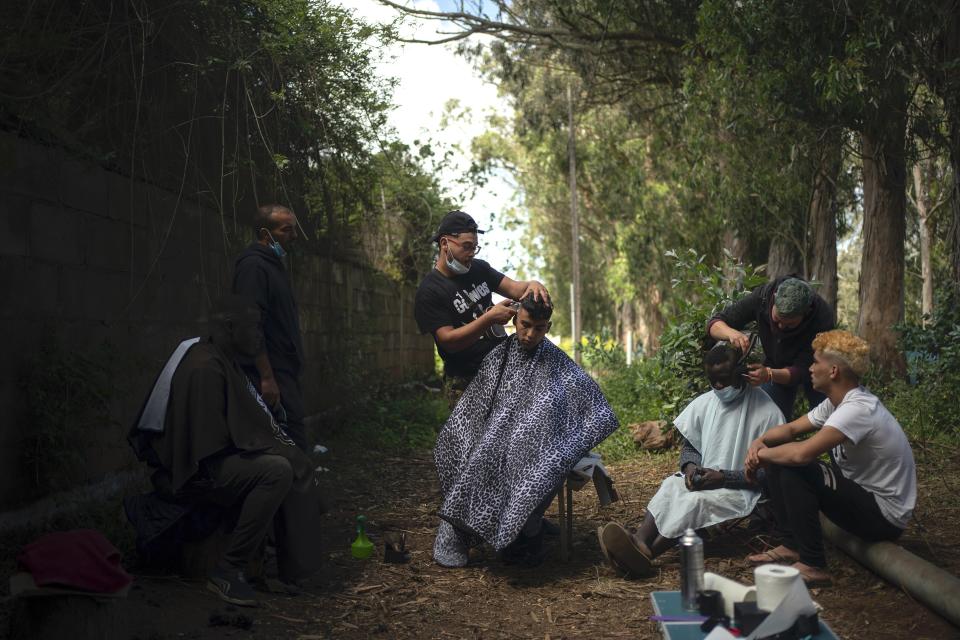 Yassime, 29, from Morocco cuts the hair of Ibrahim, 22, also from Morocco outside the Las Raices camp in San Cristobal de la Laguna, in the Canary Island of Tenerife, Spain, Friday, March 19, 2021. While Spain has been critical of its European neighbours' lack of solidarity when it comes to sharing the responsibility of migration, the country is similarly being criticized by migrants, authorities and human rights organizations on the Canary Islands where some 23,000 people arrived by sea last year and where many thousands remain on the island forcefully. (AP Photo/Joan Mateu)