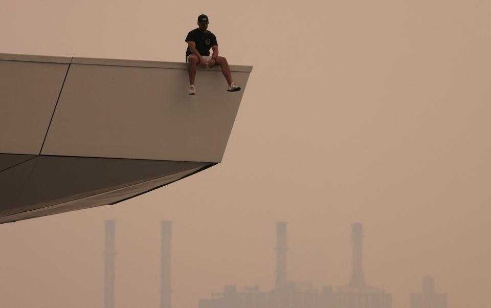 A person sits on a lookout in Long Island City in Queens, as haze and smoke caused by wildfires in Canada blanket New York City - ANDREW KELLY/REUTERS