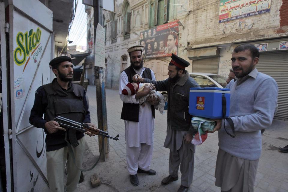 In this Feb. 9, 2014 photo, a Pakistani police man, left, stands guard as a health worker vaccinates a child against polio, in Peshawar, Pakistan. Pakistan’s beleaguered battle to eradicate polio is threatening a global, multi-billion dollar campaign to wipe out the disease worldwide. Because of Pakistan, the virus is spreading to countries that were previously polio free, say U.N. officials. “The largest poliovirus reservoir of the world,” is in Peshawar, the capital of Pakistan’s northwest Khyber Pukhtunkhwa province, which borders Afghanistan, according to the World Health Organization. (AP Photo/Mohammad Sajjad)