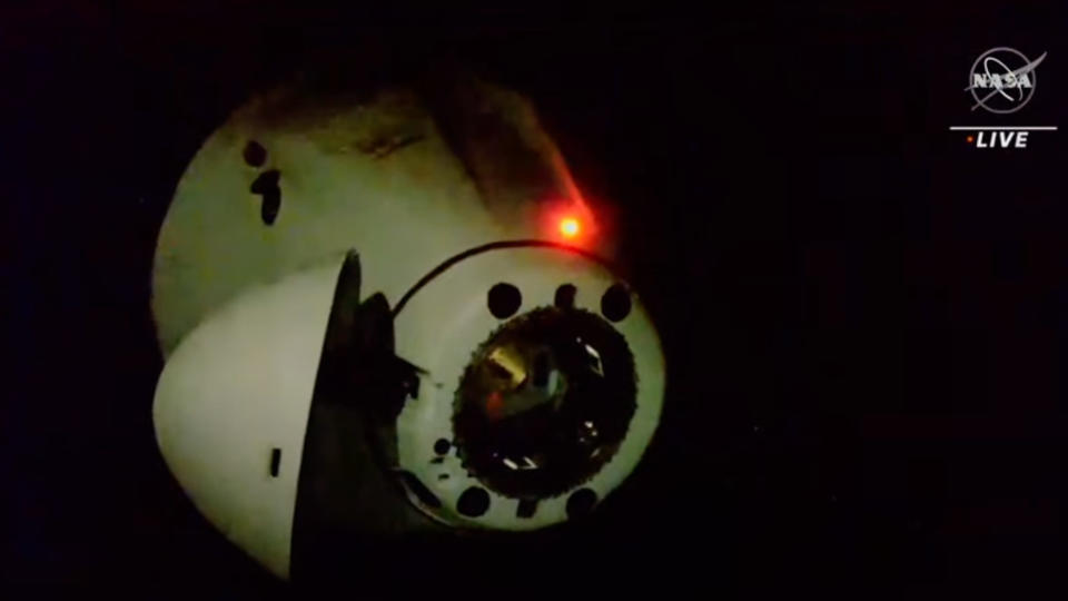 a white spacex dragon capsule backs away from the international space station with the blackness of space in the background