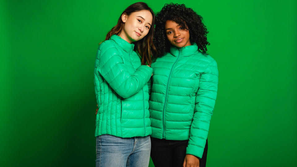 Two female friends standing infront of a green background in a studio.