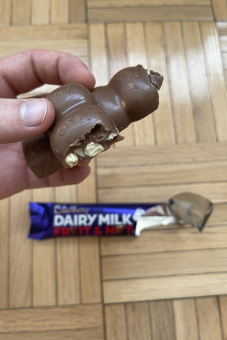 A person holding a half-eaten Cadbury Dairy Milk Fruit & Nut chocolate bar with its wrapper partly visible