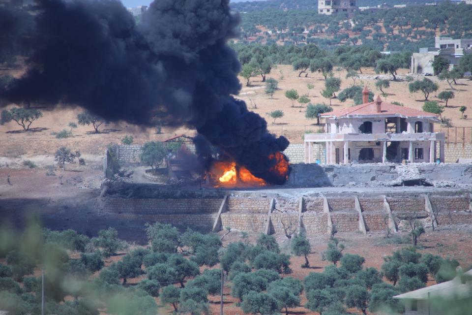 The base of a building is in flames, releasing thick black smoke into the sky.