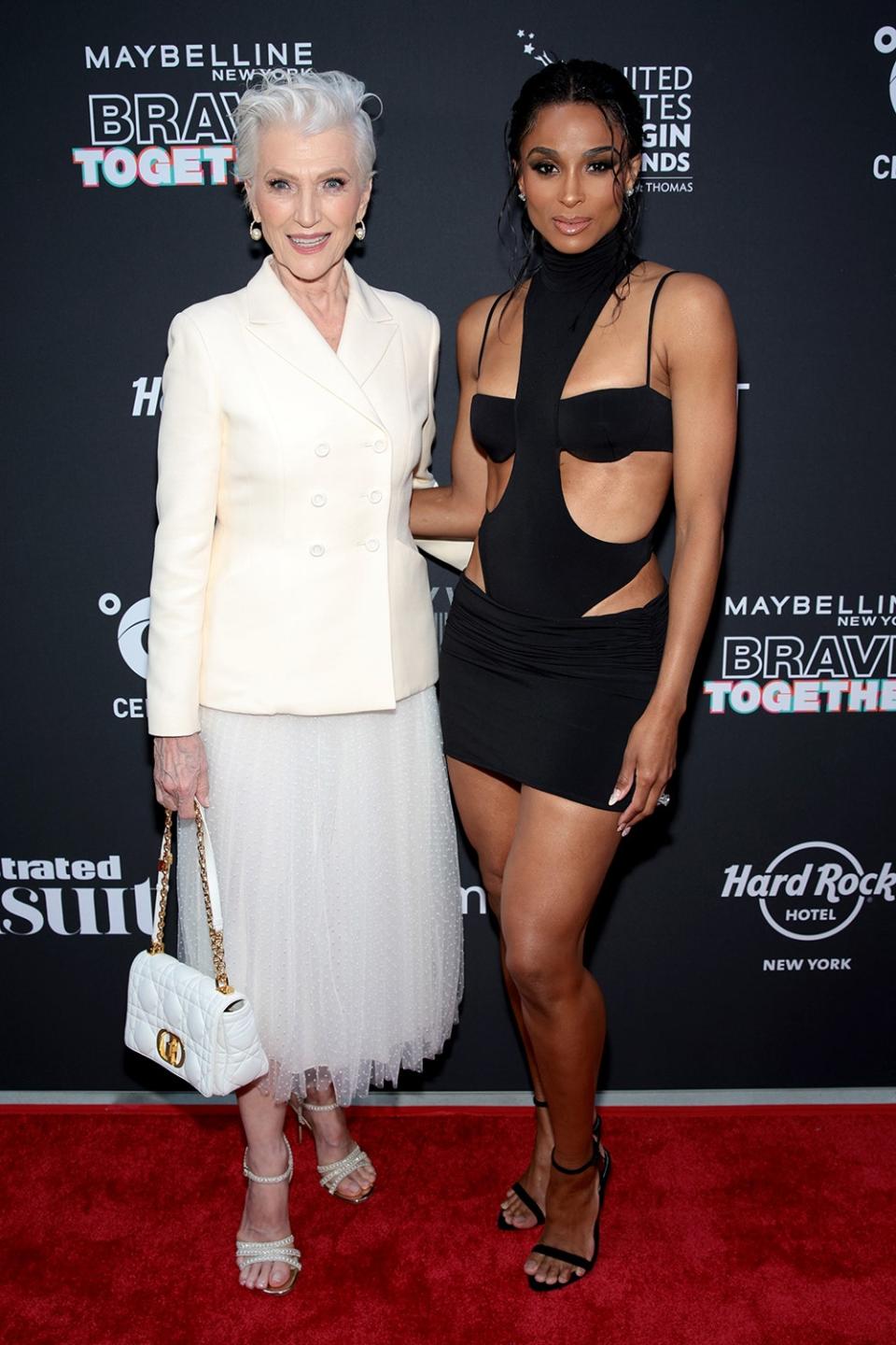 Maye Musk wearing a white blazer and a white ballerina skirt posing next to Ciara who is wearing a black cut-out dress