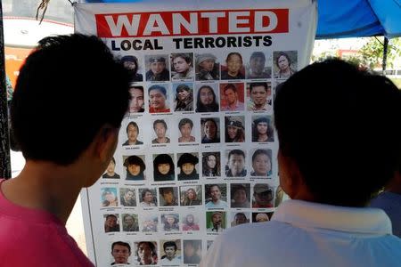 Men look at a poster issued by authorities with pictures of wanted Maute group members in Iligan, as government forces continue their assault against insurgents who have taken over large parts of Marawi City, Philippines June 24, 2017. REUTERS/Jorge Silva