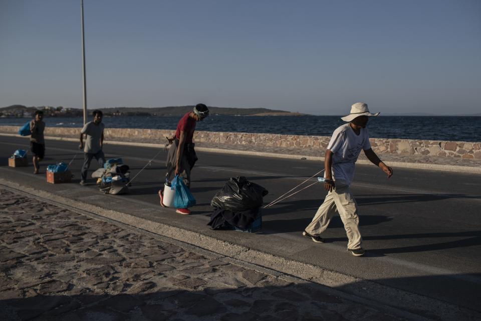 Migrants pull their belongings as they walk on a road near Mytilene town, on the northeastern island of Lesbos, Greece, Monday, Sept. 14, 2020. Greece's prime minister demanded Sunday that the European Union take a greater responsibility for managing migration into the bloc, as Greek authorities promised that 12,000 migrants and asylum-seekers left homeless after fire gutted an overcrowded camp would be moved shortly to a new tent city. (AP Photo/Petros Giannakouris)