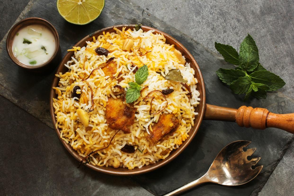 Turkey biryani in a small copper skillet with a fork and dipping sauce on a slate board