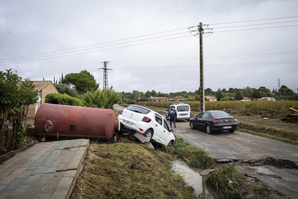 A police officer inspects a damaged car in the town of Villegailhenc, southern France, Monday, Oct.15, 2018. Flash floods tore through towns in southwest France, turning streams into raging torrents that authorities said killed several people and seriously injured at least five others. (AP Photo/Fred Lancelot)