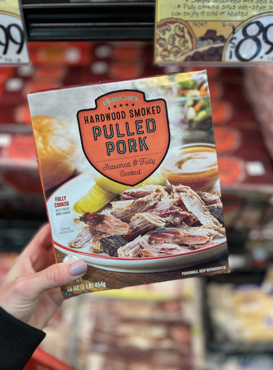 Hand holding a package of Trader Joe's Hardwood Smoked Pulled Pork in a grocery store aisle