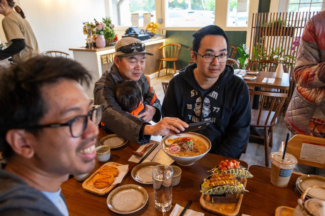 Tony Chow, left, and Hien Tran, right, accompany Ming Chow, holding his grandson, Nathan Tran, as he takes a snapshot of sushi tacos at Engawa Fusion restaurant in south Sacramento on Saturday, May 4, 2024.