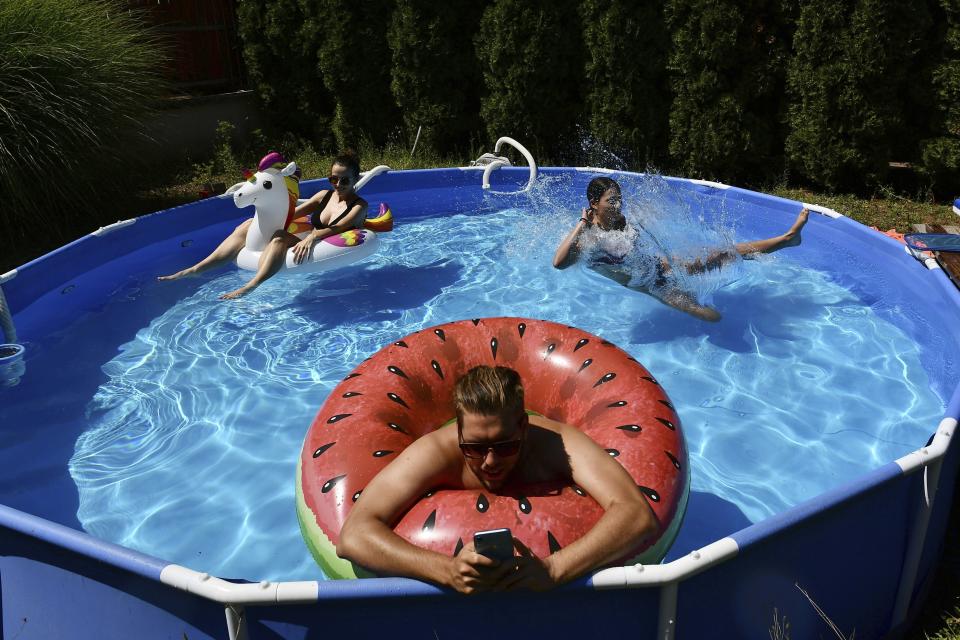 Barnabas Kantor works from the pool while his wife, Rebeka, left, and sister-in-law, Emma, cool down in Budapest, Hungary, on Aug. 4, 2022. (AP Photo/Anna Szilagyi)