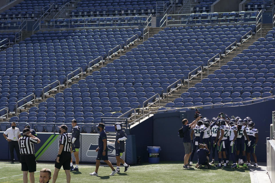 Seattle Seahawks defensive players huddle in front of empty seats at CenturyLink Field during warmups before an NFL football mock game Wednesday, Aug. 26, 2020, in Seattle. (AP Photo/Ted S. Warren)