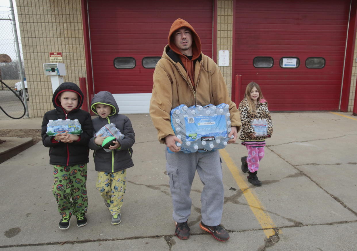 Flint resident Jerry Adkisson and his children carry water bottles from a fire station. 