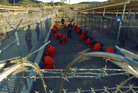 Detainees in orange jumpsuits sit in a holding area under the watchful eyes of military police during in-processing to the temporary detention facility at Camp X-Ray of Naval Base Guantanamo Bay in this January 11, 2002 file photograph. REUTERS/Stringer/Files