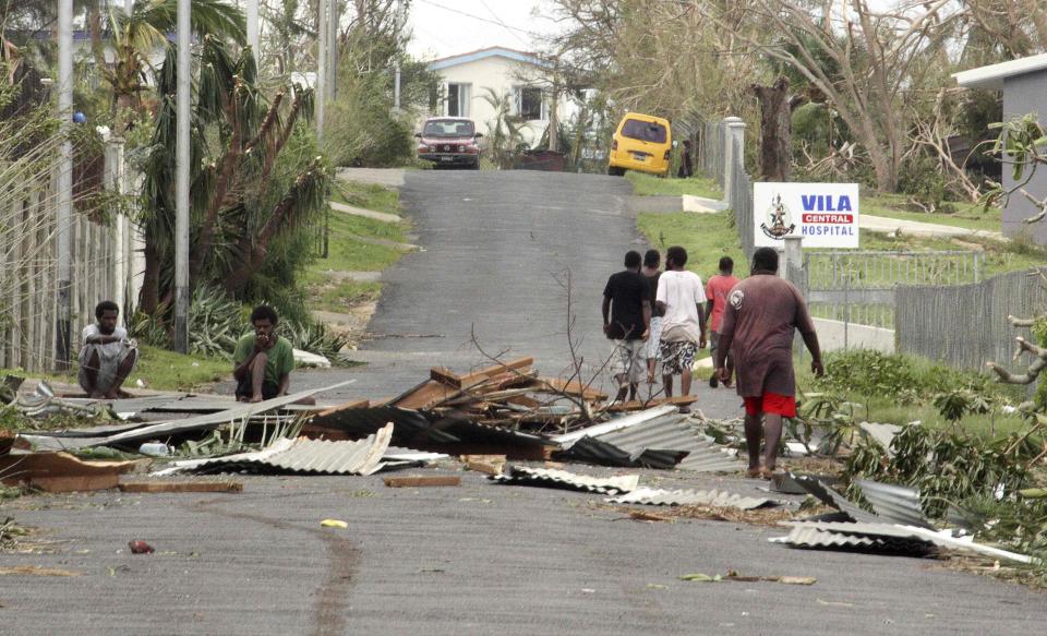 Local residents sit near debris on a road outside a hospital after Cyclone Pam hit Port Vila, the capital city of the Pacific island nation of Vanuatu