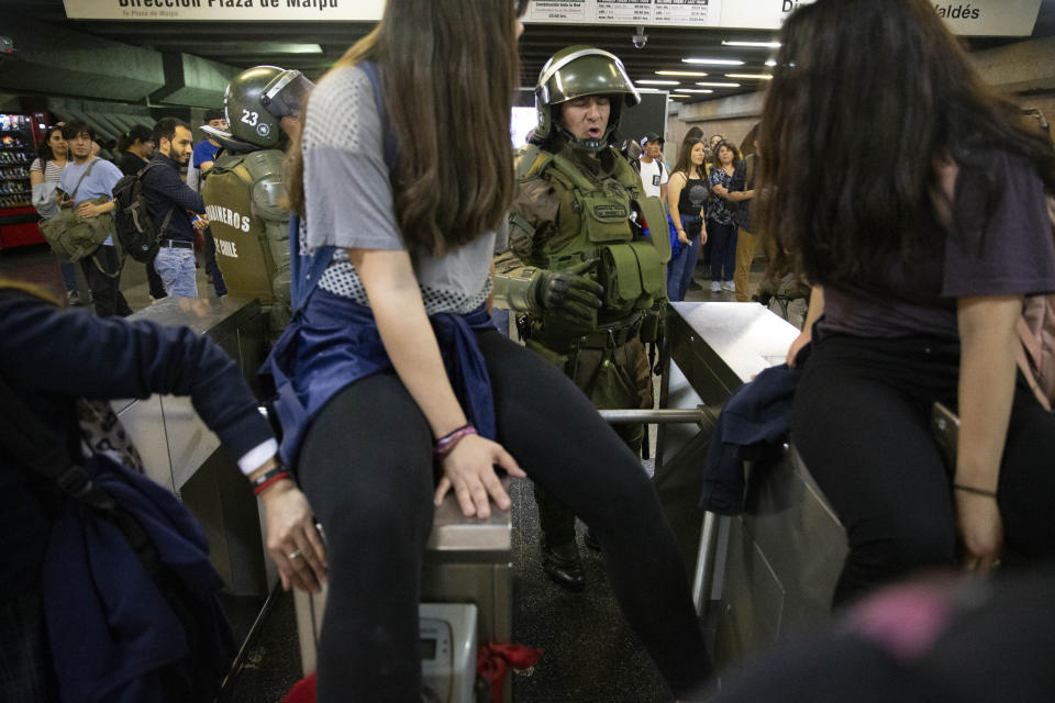 Chile's Carabineros argue with students blocking the turnstile to the subway protesting against the rising cost of subway and bus fare, in Santiago, Friday, Oct. 18, 2019. (AP Photo/Esteban Felix)