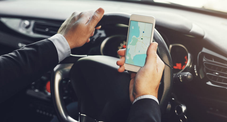 A stock image of a man is pictured using his mobile phone to look at a map while driving. NSW will be rolling out cameras to catch drivers on their mobile phones.