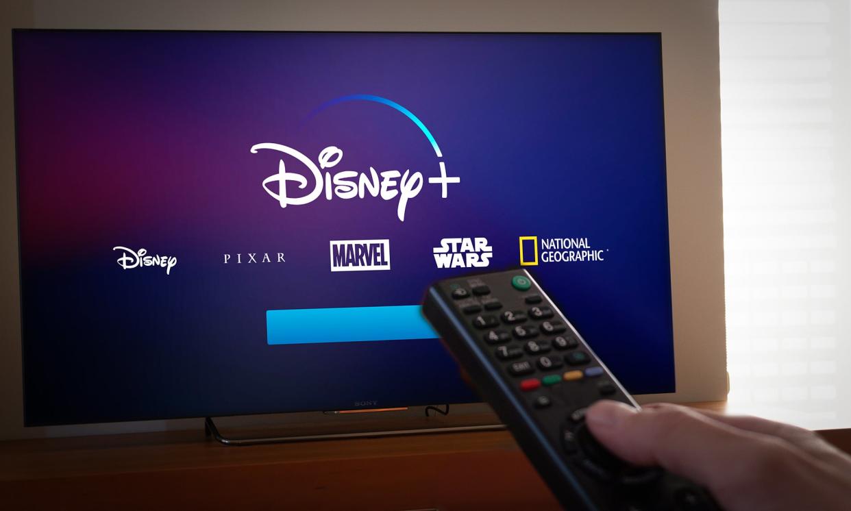  Image of Disney Plus being watched on a TV with a hand holding a remote control. 