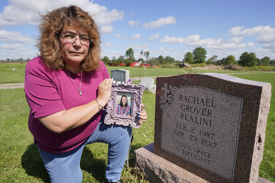 Sharon Grover holds a photograph of her daughter, Rachael, over the gravesite at Fairview Cemetery, Tuesday, Sept. 28, 2021, in Mesopotamia, Ohio. Grover believes her daughter started using prescription painkillers around 2013 but missed any signs of her addiction as her daughter, the oldest of five children, remained distanced. (AP Photo/Tony Dejak)