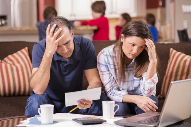 Latin descent man and woman struggle to pay their monthly bills.  They are calculating expenses versus budget income and are ups