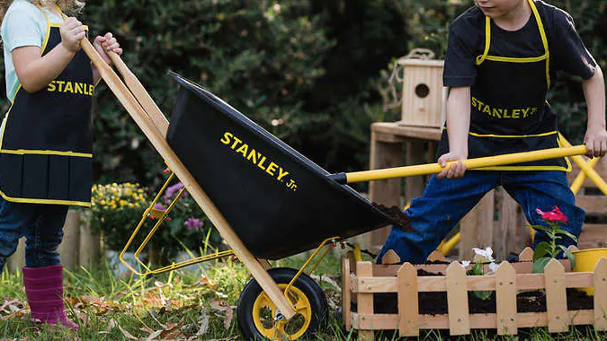 a boy and girl pushing a wheelbarrow