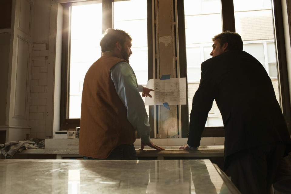 Two people standing in front of a counter with a construction plan in front of them