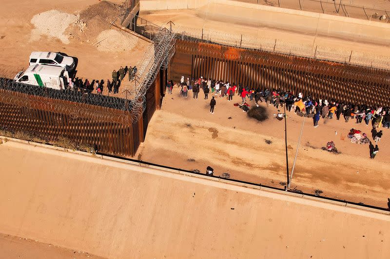 Migrants queue near the border fence after crossing the Rio Bravo river, in Ciudad Juarez