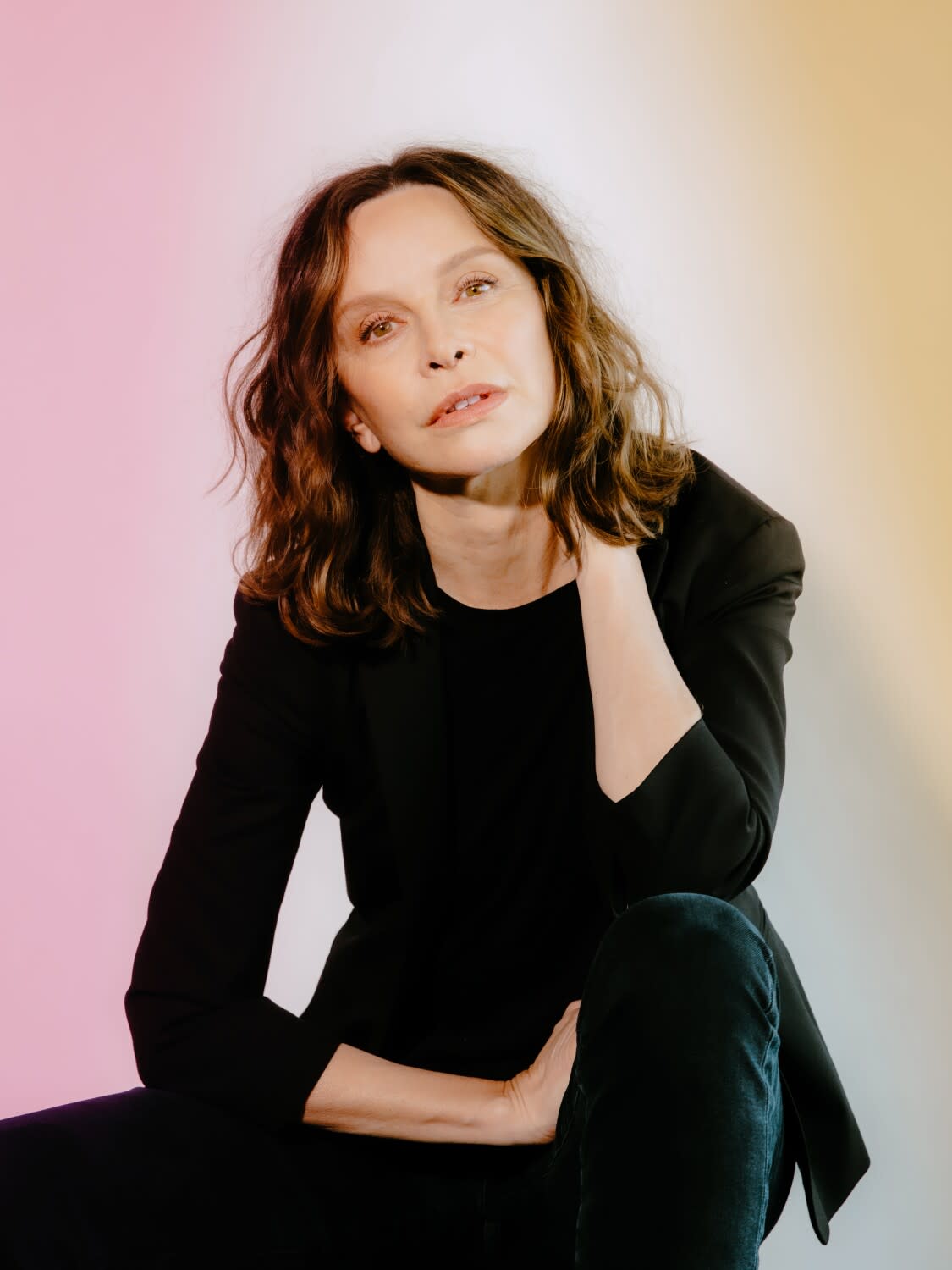 A woman in all black sits on a stool and poses