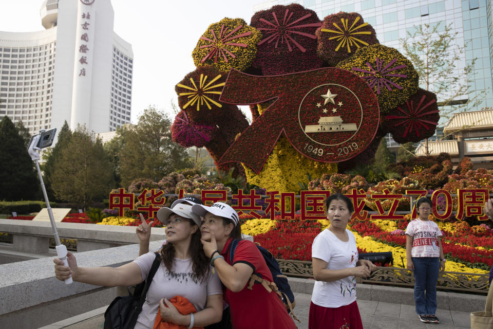 In this Saturday, Sept. 28, 2019, photo, Chinese women take a selfie near a floral decoration for the upcoming 70th anniversary of the Founding of the People's Republic of China in Beijing. Chinese President Xi Jinping has an ambitious goal for China: to achieve "national rejuvenation" as a strong and prosperous nation by 2049, which would be the 100th anniversary of Communist Party rule. One problem: U.S. President Donald Trump wants to make the United States great again too. (AP Photo/Ng Han Guan)
