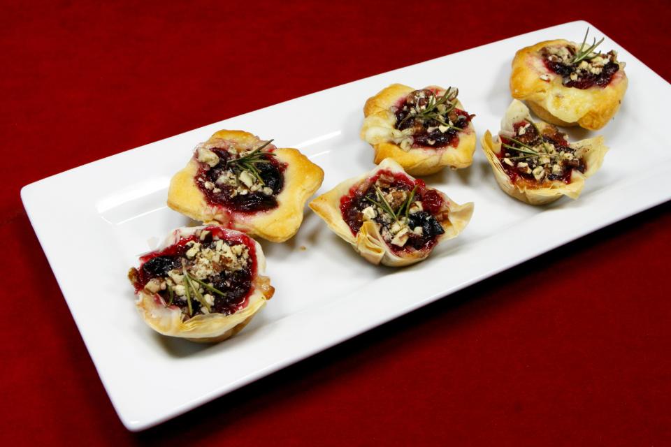 Cranberry Brie Bites are dough filled with chunks of brie and a tangy cranberry sauce and topped with chopped pecans and a sprig of fresh rosemary. Here, some were made using the crescent roll dough called for in the recipe, while others are in phyllo shells.